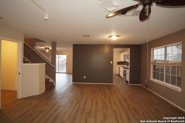 unfurnished living room featuring dark wood-style flooring, ceiling fan, and stairs