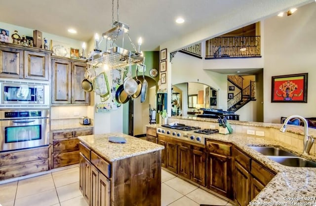kitchen featuring arched walkways, light stone countertops, a sink, light tile patterned floors, and stainless steel appliances