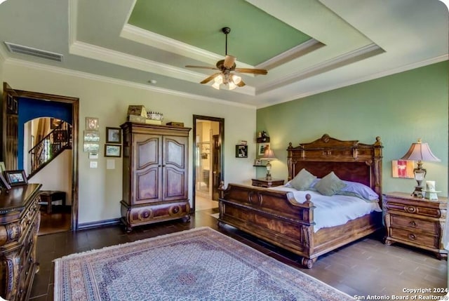 bedroom featuring ensuite bathroom, a tray ceiling, wood finished floors, and visible vents