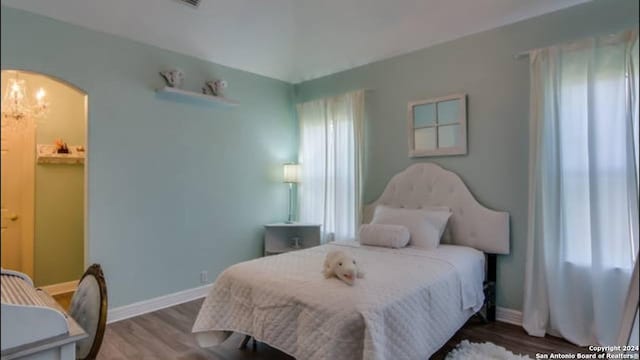bedroom with arched walkways, baseboards, and wood finished floors
