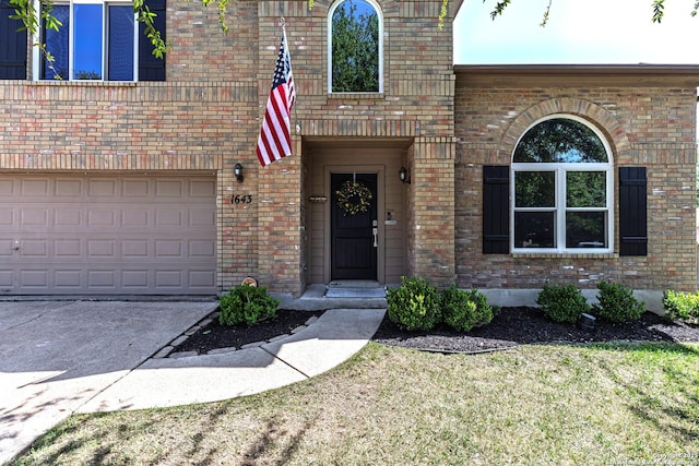 property entrance with brick siding, an attached garage, a lawn, and concrete driveway