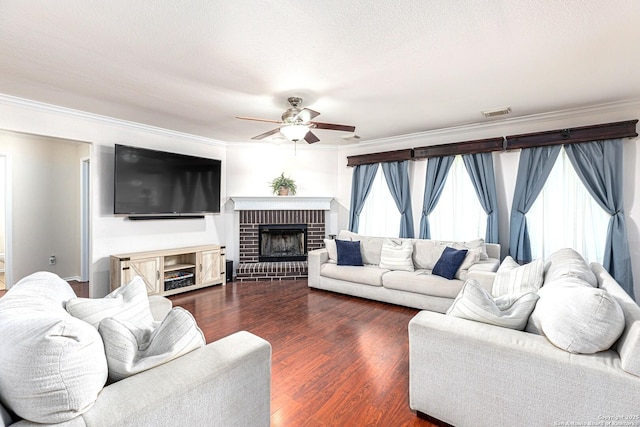 living area featuring dark wood-style floors, visible vents, a ceiling fan, a fireplace, and ornamental molding