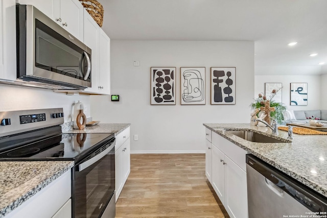 kitchen featuring a sink, light wood-type flooring, light stone countertops, appliances with stainless steel finishes, and white cabinetry