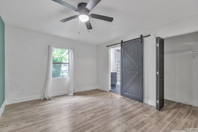 unfurnished bedroom with a barn door, wood finished floors, baseboards, and a closet
