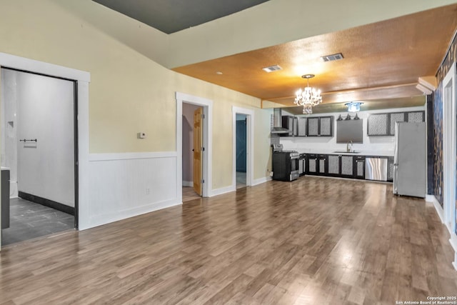 unfurnished living room with a sink, a chandelier, wood finished floors, a wainscoted wall, and baseboards