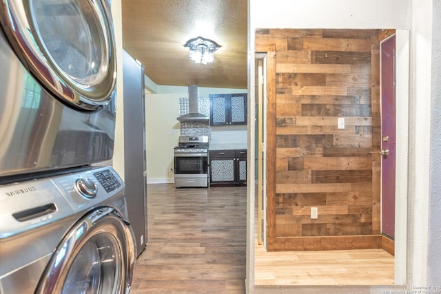 laundry room featuring stacked washer and clothes dryer, wood finished floors, and baseboards