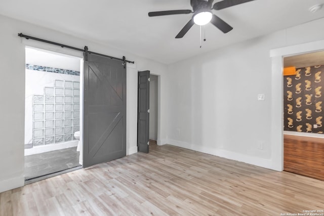 empty room with a barn door, wood finished floors, a ceiling fan, baseboards, and a smoke detector