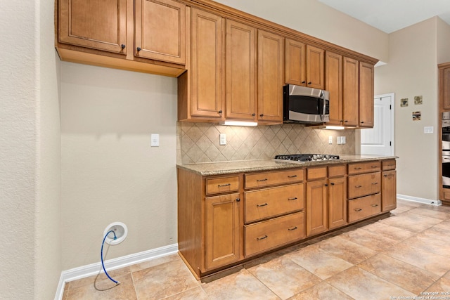 kitchen with backsplash, brown cabinets, baseboards, and stainless steel appliances