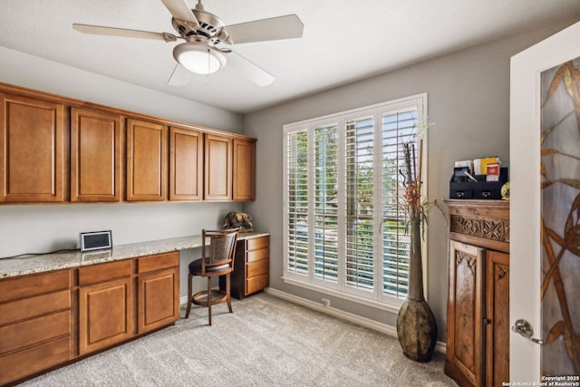 office area with built in study area, light carpet, a ceiling fan, and baseboards