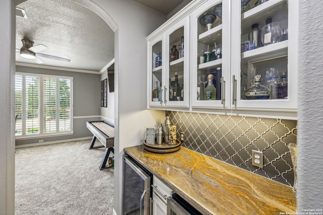 bar with wine cooler, arched walkways, a textured ceiling, a ceiling fan, and carpet floors