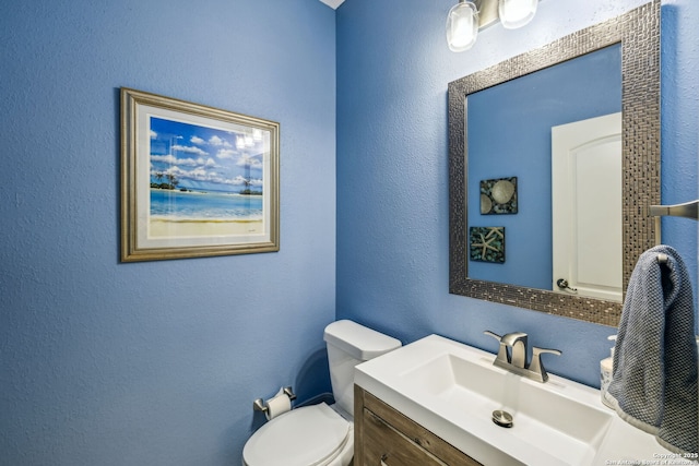 bathroom with a textured wall, toilet, and vanity