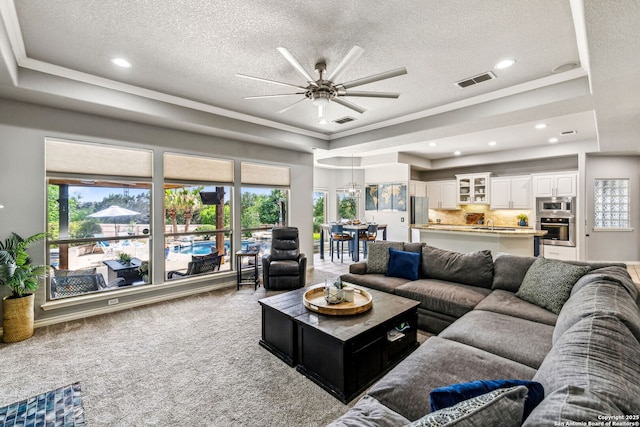 carpeted living area featuring a raised ceiling, visible vents, a textured ceiling, and ceiling fan
