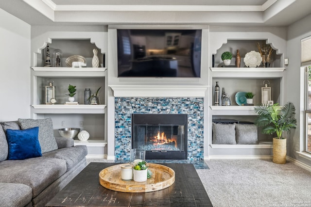 carpeted living area featuring a raised ceiling, crown molding, built in features, and a fireplace