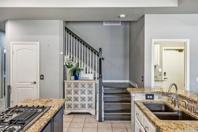 kitchen featuring stainless steel gas stovetop, light stone counters, visible vents, a sink, and white cabinetry