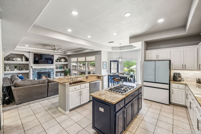 kitchen featuring a kitchen island with sink, a sink, a ceiling fan, appliances with stainless steel finishes, and a raised ceiling