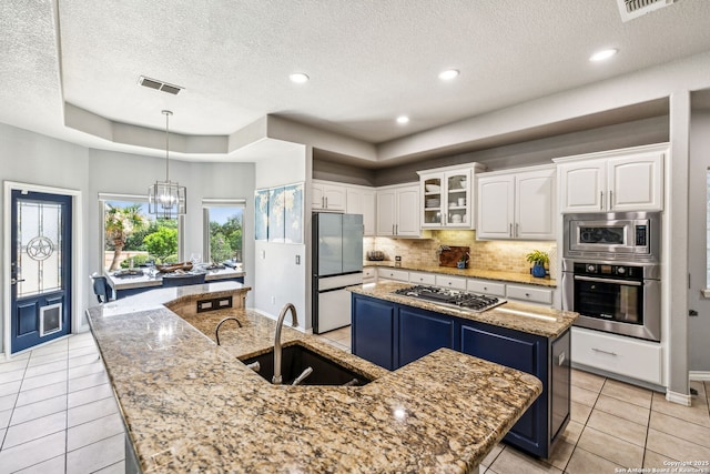 kitchen featuring stainless steel appliances, a raised ceiling, visible vents, a sink, and a kitchen island with sink