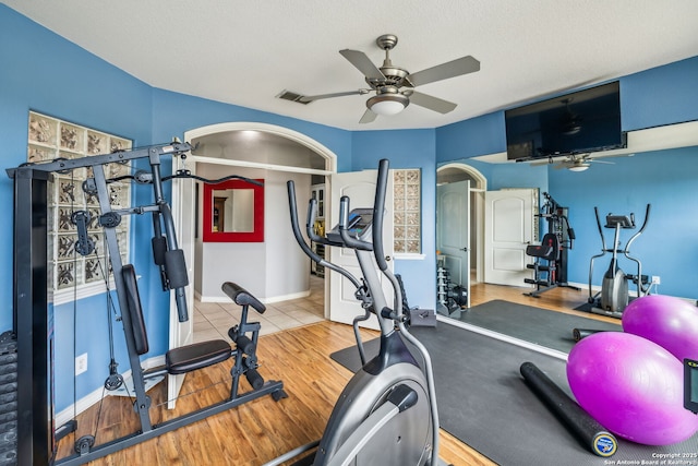 exercise area with wood finished floors, visible vents, arched walkways, baseboards, and ceiling fan