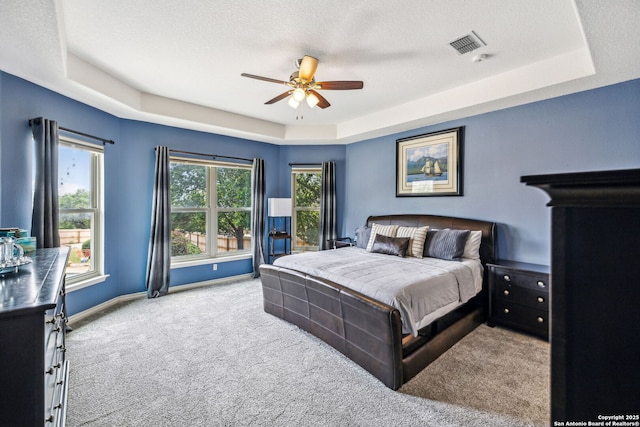 carpeted bedroom with a tray ceiling, visible vents, a ceiling fan, and baseboards