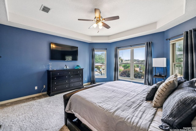 bedroom featuring a raised ceiling, visible vents, carpet floors, baseboards, and multiple windows