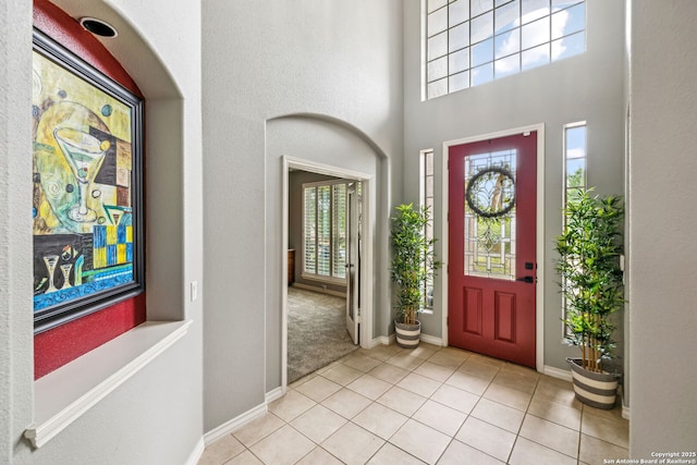 foyer entrance featuring baseboards, a towering ceiling, and light tile patterned floors