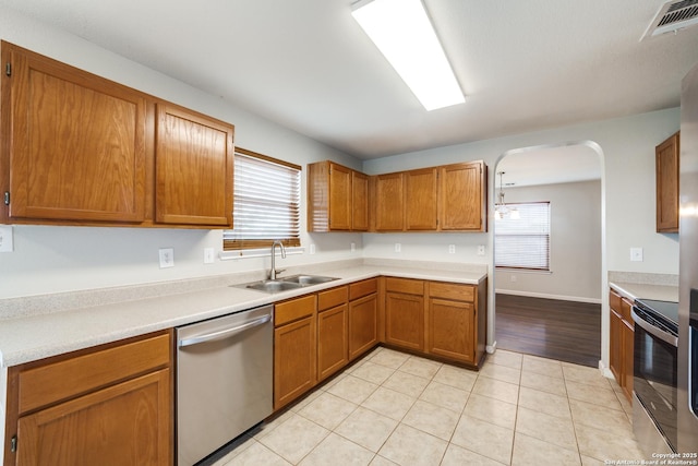 kitchen featuring stainless steel appliances, arched walkways, a sink, and brown cabinetry