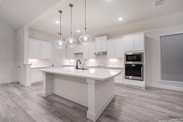 kitchen with built in microwave, under cabinet range hood, a sink, decorative backsplash, and stainless steel oven