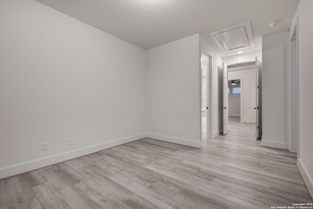 empty room with attic access, baseboards, light wood-style floors, and a textured ceiling