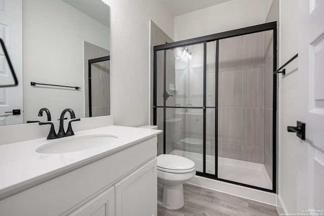 full bathroom with toilet, wood finished floors, vanity, and a stall shower