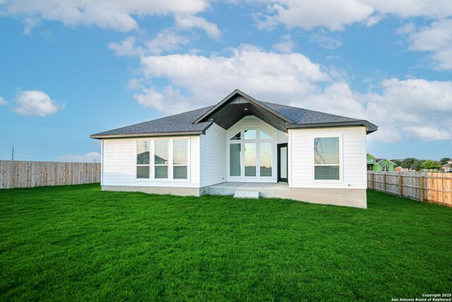 back of house with a fenced backyard, roof with shingles, a patio area, and a yard