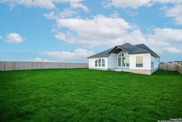 rear view of house with a lawn, a fenced backyard, and roof with shingles
