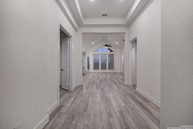 hallway with lofted ceiling, a textured wall, wood finished floors, and visible vents
