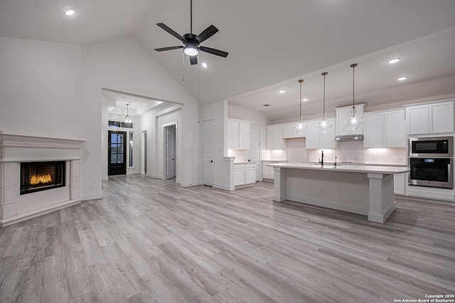 kitchen featuring built in microwave, under cabinet range hood, light countertops, stainless steel oven, and open floor plan