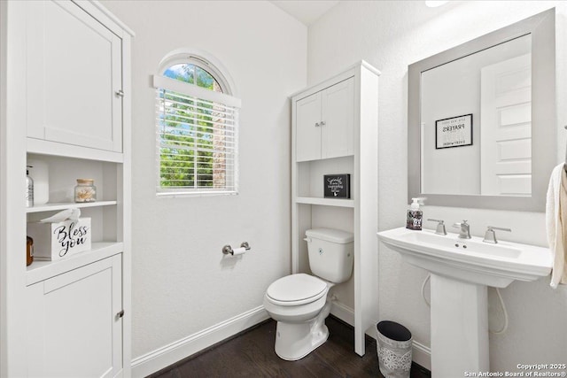 half bath featuring baseboards, wood finished floors, a sink, and toilet