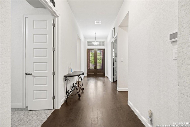 hall featuring dark wood finished floors, a textured wall, visible vents, french doors, and baseboards
