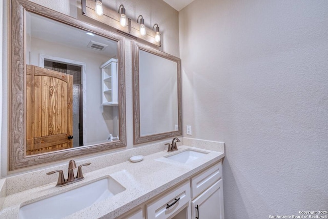 bathroom featuring a textured wall, a sink, double vanity, and visible vents