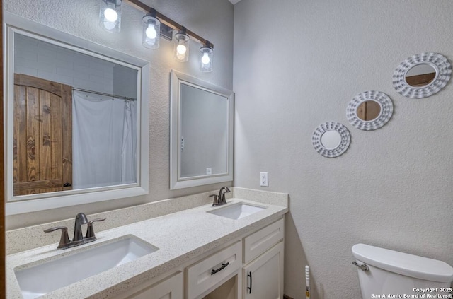 bathroom featuring a textured wall, a sink, double vanity, and toilet