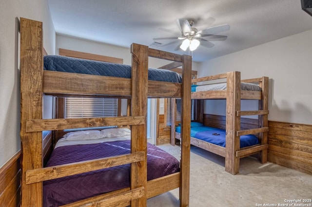 bedroom with wood walls, a ceiling fan, a wainscoted wall, and carpet