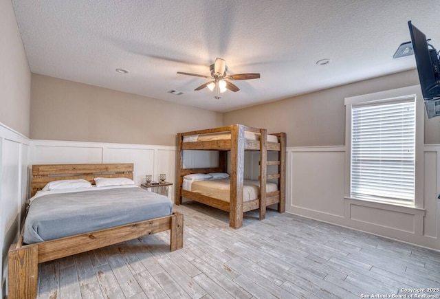 67 Stepping Stone, Concan, TX 78838 - bedroom with light wood finished floors, a wainscoted wall, a textured ceiling, and a decorative wall