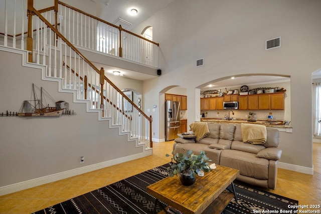 living room featuring visible vents, arched walkways, light tile patterned floors, and stairway