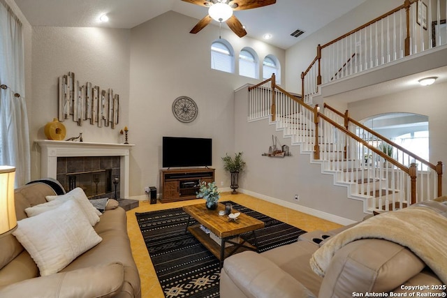 living room featuring visible vents, stairs, ceiling fan, high vaulted ceiling, and a tile fireplace