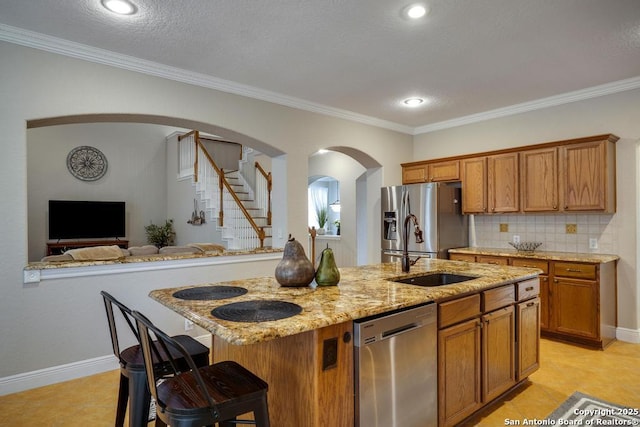 kitchen with arched walkways, brown cabinets, light stone counters, a sink, and stainless steel appliances