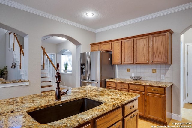 kitchen with a sink, stainless steel fridge with ice dispenser, brown cabinetry, and arched walkways