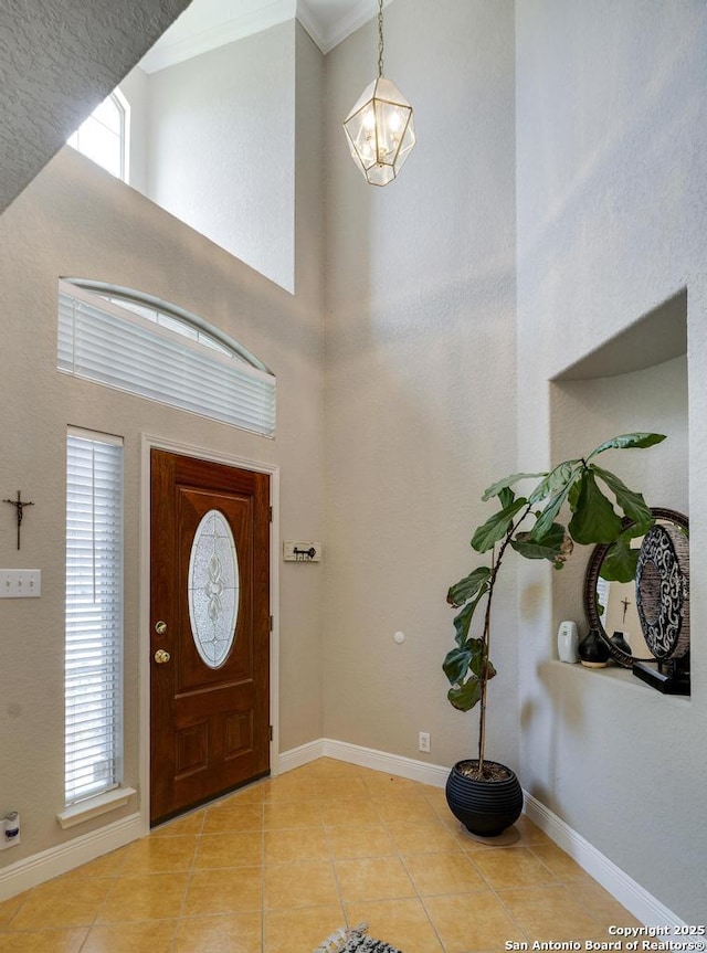 entrance foyer with crown molding, a high ceiling, a chandelier, and light tile patterned floors