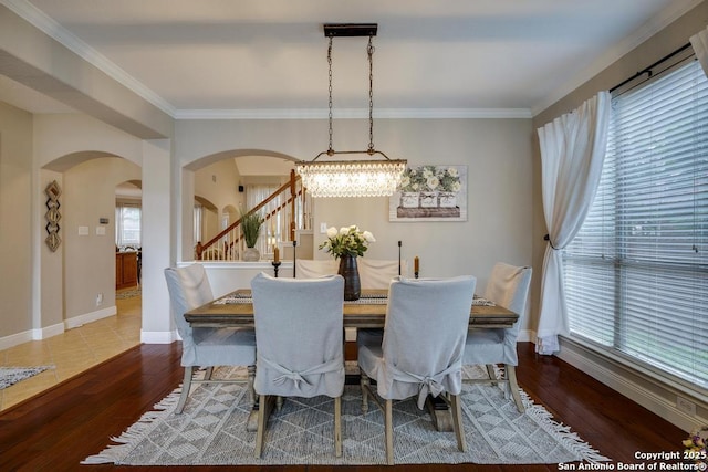 dining room featuring arched walkways, baseboards, wood finished floors, ornamental molding, and stairway