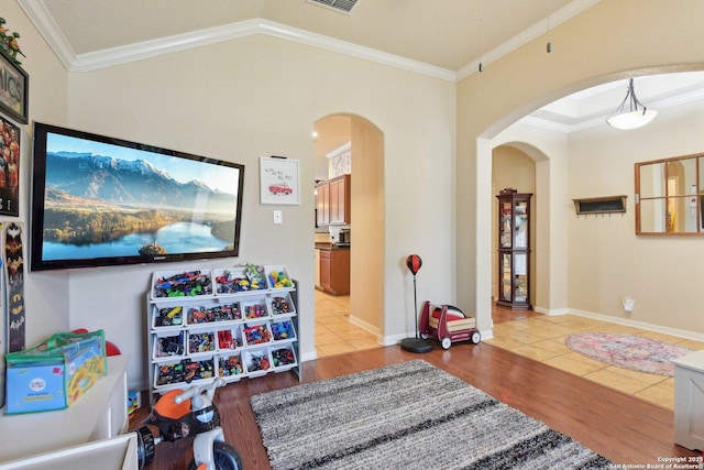 recreation room featuring arched walkways, crown molding, light wood-style floors, and lofted ceiling