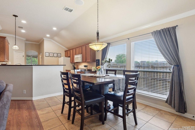 dining space featuring lofted ceiling, visible vents, light tile patterned flooring, crown molding, and baseboards