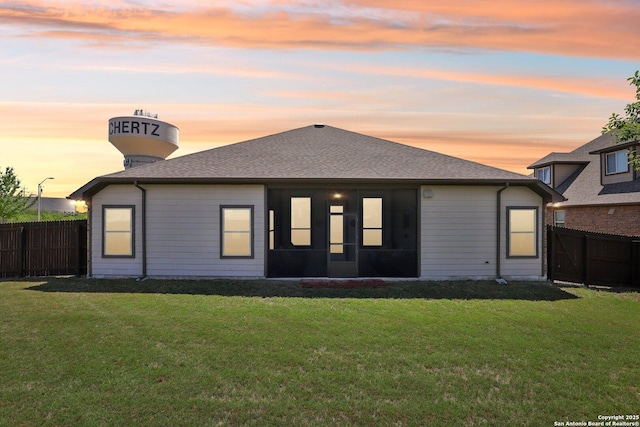 rear view of property featuring a fenced backyard, roof with shingles, a yard, and a sunroom