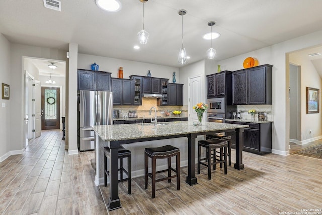 kitchen featuring stainless steel appliances, a sink, visible vents, decorative backsplash, and a breakfast bar