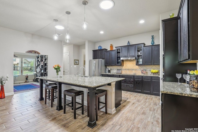 kitchen featuring a sink, freestanding refrigerator, backsplash, a breakfast bar, and under cabinet range hood