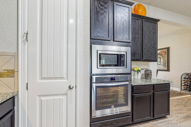 kitchen featuring light stone counters, decorative backsplash, a warming drawer, light wood finished floors, and appliances with stainless steel finishes